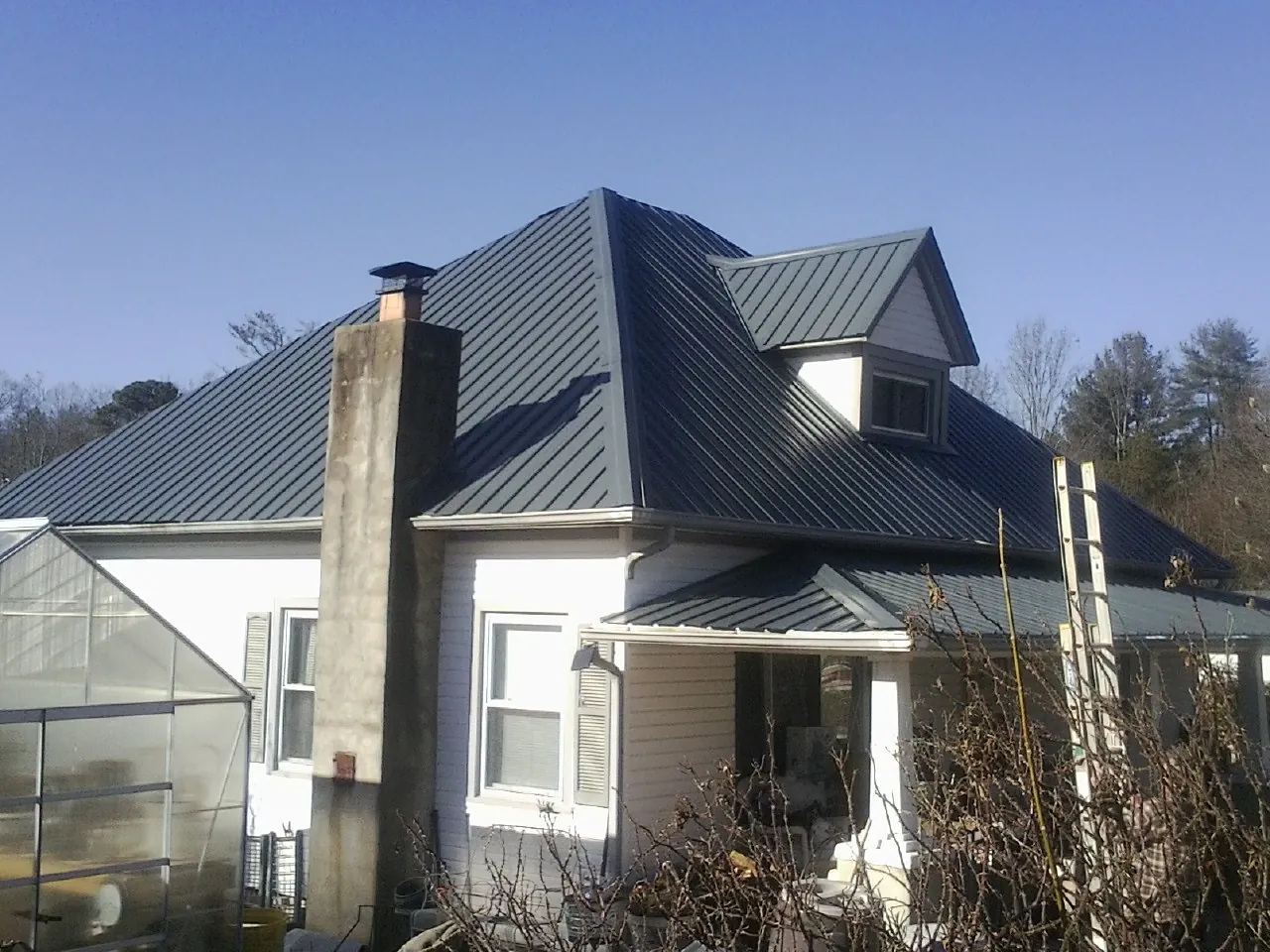 Dark blue standing seam metal roof on a white farmhouse with dormer — Slate & Tile Roof Repair by Roofing Brothers in Buena Vista