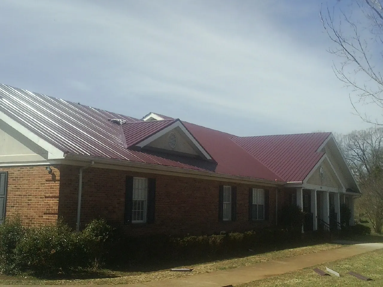 Red metal roof with gabled entries on a long brick building, from a Hail Damage Roof Repair job in Buena Vista