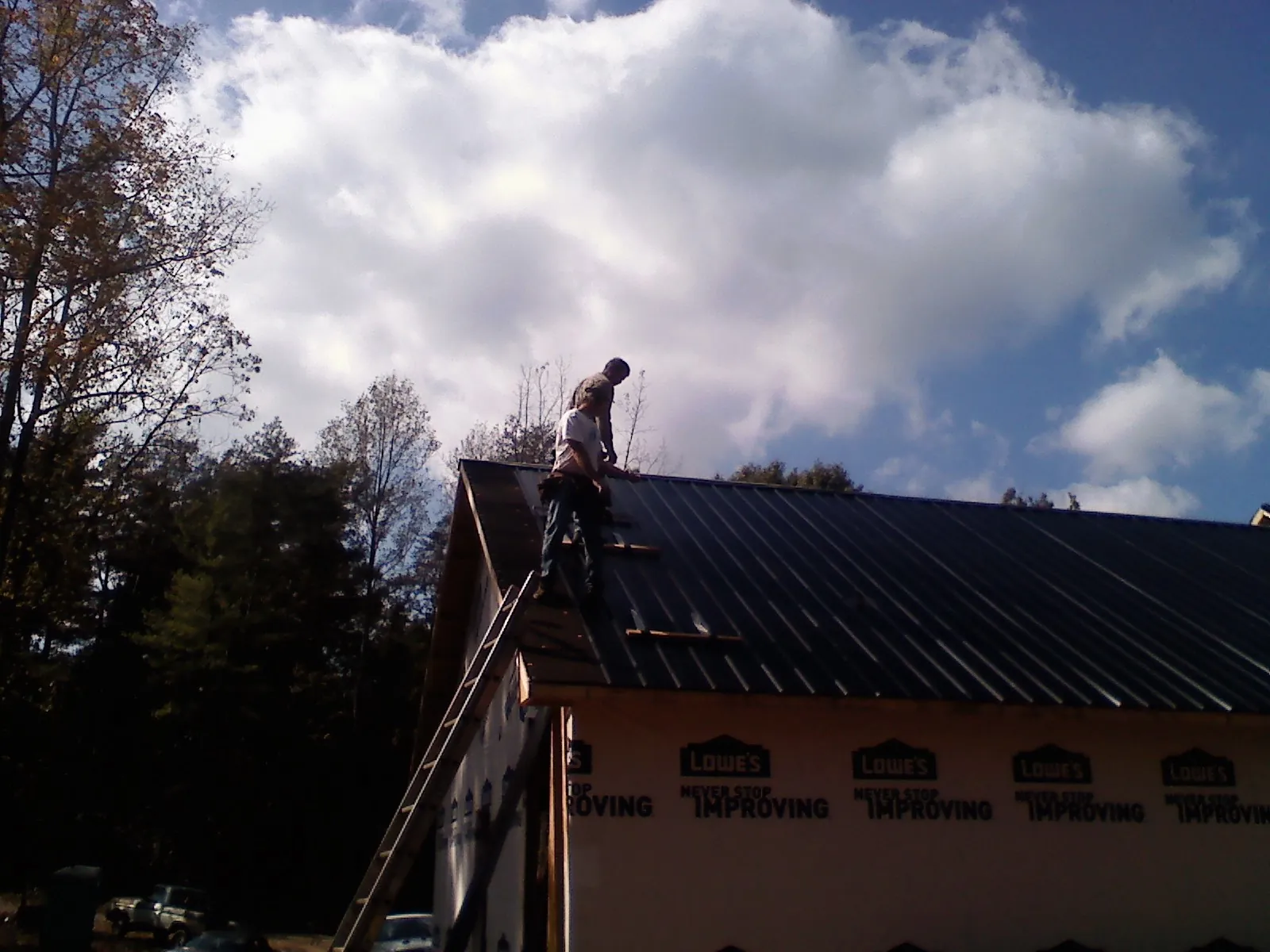 Roofer fastening dark metal panels high against a cloudy sky, from a Roof Inspection job in Buena Vista